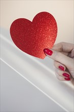 Close up of woman's fingers with red nail polish holding red heart.
