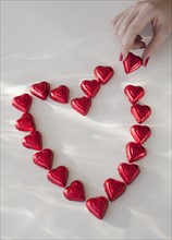 Close up of woman's hand with red nail polish making heart shape from chocolates.