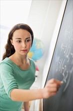 Teenage girl (14-15) writing on blackboard.