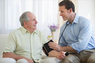 Smiling man taking senior man's blood pressure.