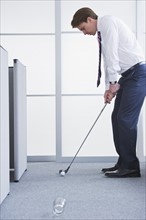 Businessman playing golf at office. Photo : Daniel Grill