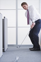 Businessman playing golf at office. Photo : Daniel Grill