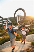 USA, California, Laguna Beach, Two men carrying bikes up hill.