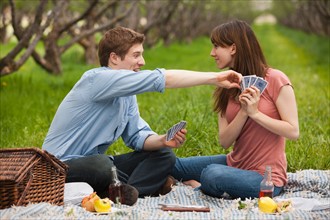 USA, Utah, Provo, Young couple playing cards during picnic in orchard. Photo : Mike Kemp