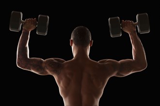 Rear view of muscular man exercising with dumbbells. Photo : Mike Kemp