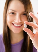 Portrait of smiling young woman holding pill. Photo : Jamie Grill Photography