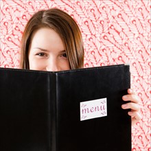 Portrait of smiling young woman holding restaurant menu in front of face. Photo : Jamie Grill