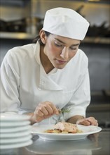 Female cook preparing food in commercial kitchen.