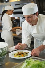 Chef and cook preparing food in commercial kitchen.