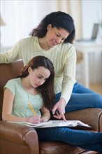Mother helping to teenage girl (14-15) doing homework.