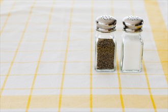 Salt and pepper shakers on checked tablecloth.