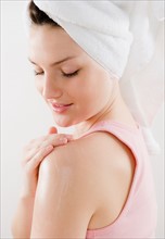 Young woman applying moisturizer on shoulder. Photo : Jamie Grill Photography