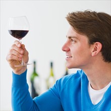 Young man examining red wine. Photo : Daniel Grill