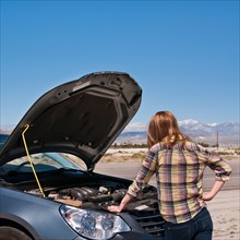 USA, California, Palm Springs, Woman standing in front of broken car in desert. Photo : Daniel