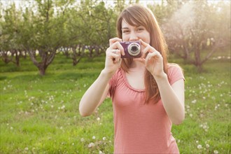 USA, Utah, Provo, Young woman holding digital camera in orchard. Photo : Mike Kemp