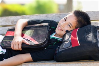 Portrait of school boy (12-13) with bags on bench. Photo : Noah Clayton