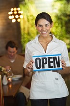 Smiling waitress in restaurant showing "open sign".