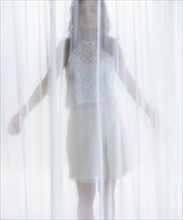 Portrait of young woman behind curtain.