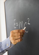Close-up of man's hand writing theory of relativity formula on blackboard.