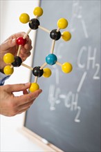 Close-up of man's hands holding molecule model, blackboard in background.