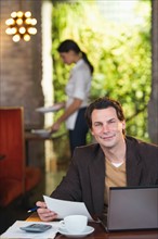 Owner working with laptop in restaurant with waitress in background.