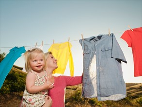 Mother with daughter (12-17 months) hanging laundry on clothesline .