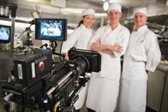 Three chefs posing in kitchen, camera in foreground.