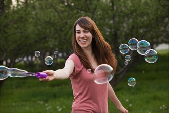 Young woman blowing bubbles in orchard. Photo : Mike Kemp