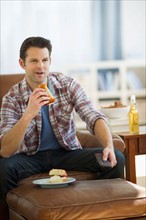 Man watching tv and eating sandwich.