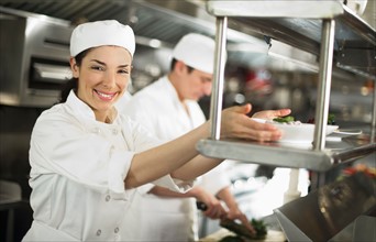 Chefs preparing food, woman looking at camera and smiling.