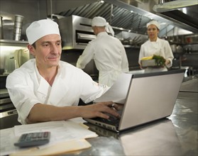 Chefs preparing food, one working on laptop.
