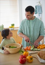 Daughter (8-9) and father preparing vegetables in kitchen.