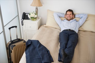 Businessman relaxing on bed in hotel room.