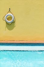 Lifebelt hanging on yellow wall by swimming pool.