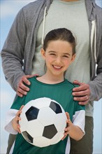 Girl (8-9) holding soccer ball, with father behind.