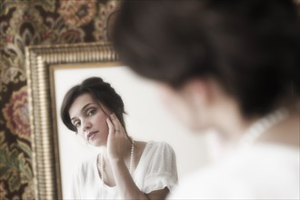 Old-fashioned young woman looking at mirror reflection.