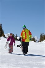 USA, Colorado, Telluride, Father and daughter (10-11) walking with snowboards in winter scenery.