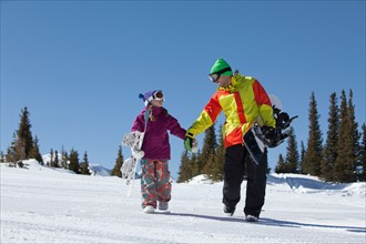 USA, Colorado, Telluride, Father and daughter (10-11) walking with snowboards in winter scenery.