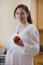 Portrait of expecting mother holding apple. Photo : Rob Lewine