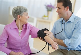 Smiling man taking senior woman's blood pressure.