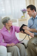 Smiling man taking senior woman's blood pressure.