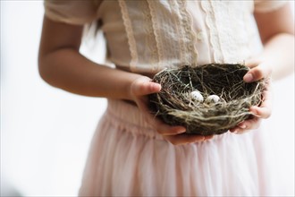 Girl (8-9) holding nest with small eggs.