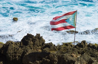 Puerto Rico, Old San Juan, Puerto Rican flag on rock with sea in background.