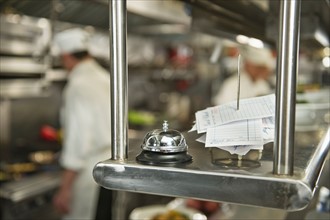 Chefs preparing food in kitchen, focus on service bell on foreground.