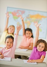 Four girls (6-9) raising hands in classroom.
