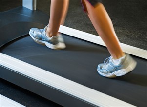 Low section of woman walking on treadmill.