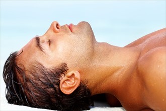 Profile of young guy lying on the beach. Photo : momentimages