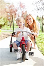Mother and son (2-3) riding on tricycle in park. Photo : Take A Pix Media