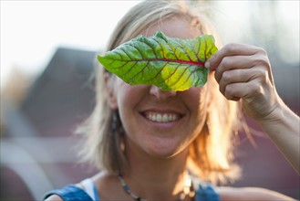 Smiling woman holding leaf in front of her face. Photo : Noah Clayton