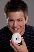 Portrait of teenage boy (16-17) with donut, studio shot. Photo: Rob Lewine